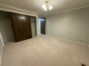 Unfurnished bedroom with a textured ceiling, a chandelier, light carpet, ornamental molding, and a closet