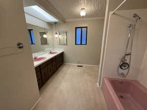 Bathroom featuring ornamental molding, shower / bathtub combination, double vanity, and a textured ceiling