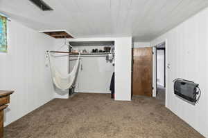 Unfurnished bedroom featuring carpet flooring, heating unit, a closet, wood ceiling, and wooden walls