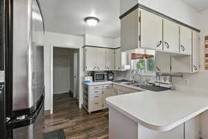 Kitchen featuring freestanding refrigerator, light countertops, dark wood-style flooring, a peninsula, and stainless steel microwave