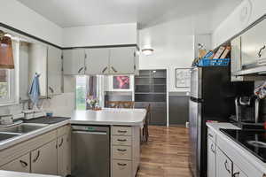 Kitchen with stainless steel dishwasher, black electric cooktop, a peninsula, light countertops, and dark wood-style floors