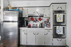 Kitchen featuring appliances with stainless steel finishes, extractor fan, light countertops, and white cabinetry