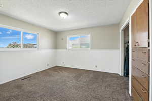 Unfurnished bedroom featuring a wainscoted wall, a textured ceiling, and dark carpet