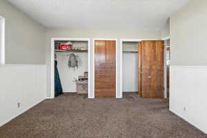 Unfurnished bedroom with two closets, a wainscoted wall, carpet floors, and a textured ceiling