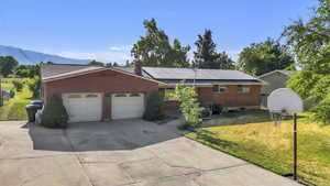 Single story home featuring a front yard, concrete driveway, solar panels, a garage, and a mountain view