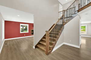 Stairs featuring wood finished floors, a glass covered fireplace, plenty of natural light, recessed lighting, and a towering ceiling