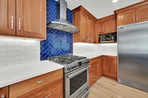 Kitchen featuring stainless steel appliances, wall chimney exhaust hood, decorative backsplash, cherry wood cabinets, and recessed lighting