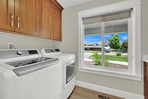 Laundry area with cabinet space, separate washer and dryer, and light wood-style flooring