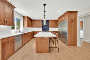Kitchen featuring appliances with stainless steel finishes, cherry wood cabinets, range hood, a breakfast bar area, and light wood finished floors