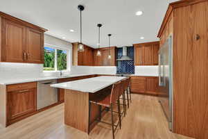 Kitchen with stainless steel appliances, wall chimney exhaust hood, light wood-style flooring, cherry wood cabinets, and a breakfast bar