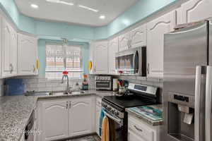 Kitchen featuring appliances with stainless steel finishes, white cabinetry, decorative backsplash, recessed lighting, and a textured ceiling