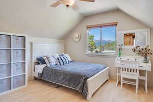 Bedroom with light wood-style flooring, lofted ceiling, a ceiling fan, and a textured ceiling