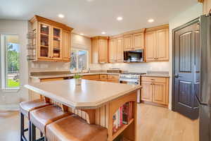 Kitchen featuring stainless steel appliances, light wood finished floors, light countertops, recessed lighting, and a kitchen breakfast bar