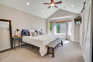 Bedroom with lofted ceiling, light colored carpet, recessed lighting, a barn door, and a ceiling fan