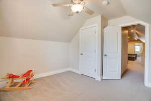 Bonus room with lofted ceiling, light colored carpet, and ceiling fan