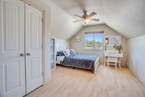 Bedroom featuring wood finished floors, a textured ceiling, lofted ceiling, and a ceiling fan
