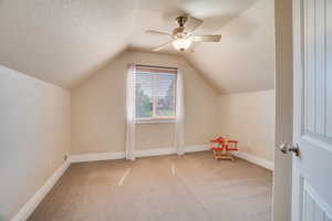 Bonus room featuring carpet flooring, lofted ceiling, ceiling fan, and a textured ceiling
