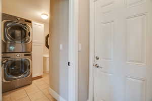 Washroom with estacked washer and dryer, cabinet space, and light tile patterned flooring