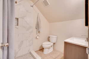 Bathroom with lofted ceiling, a tile shower, vanity, and tile patterned floors