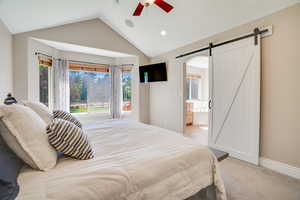 Bedroom with a barn door, vaulted ceiling, recessed lighting, light colored carpet, and ensuite bath