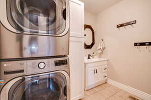Washroom with estacked washer and dryer, cabinet space, and light tile patterned floors