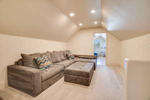 Carpeted living area featuring vaulted ceiling, recessed lighting, and a textured ceiling