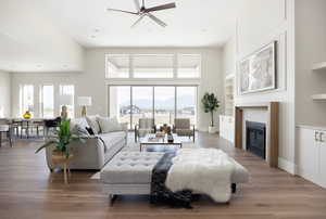Living area with a ceiling fan, light wood-style floors, a tiled fireplace, a mountain view, and a high ceiling