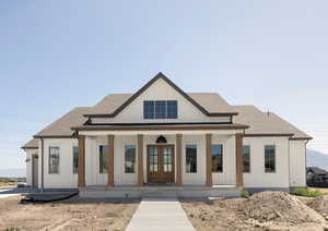 Modern inspired farmhouse with covered porch, board and batten siding, french doors, roof with shingles, and brick siding