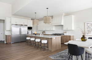 Kitchen featuring stainless steel appliances, custom exhaust hood, a kitchen breakfast bar, wood finished floors, and a kitchen island with sink