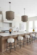 Kitchen featuring white cabinetry, light wood-style floors, backsplash, light countertops, and a kitchen breakfast bar