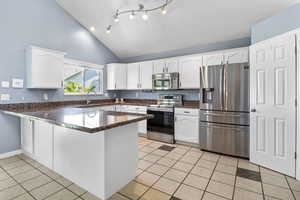 Kitchen featuring appliances with stainless steel finishes, a peninsula, white cabinetry, light tile patterned floors, and high vaulted ceiling