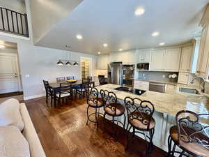 Kitchen with appliances with stainless steel finishes, a peninsula, light stone countertops, a breakfast bar area, and dark wood-style flooring