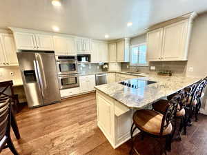 Kitchen featuring stainless steel appliances, a peninsula, light wood-style floors, a kitchen bar, and light stone counters