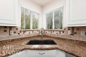 Kitchen featuring backsplash, dark stone countertops, and white cabinetry