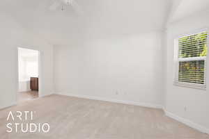Primary bedroom with light colored carpet, a ceiling fan, vaulted ceiling, and connected bathroom