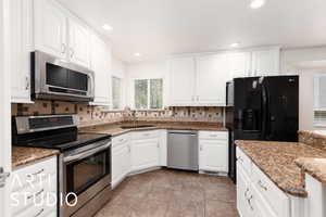 Kitchen featuring stainless steel appliances, white cabinetry, backsplash, dark stone countertops, and recessed lighting