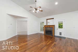 Unfurnished living room featuring dark wood-style floors, a tiled fireplace, vaulted ceiling, plenty of natural light, and recessed lighting