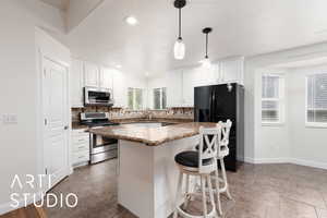 Kitchen featuring a kitchen bar, stainless steel appliances, hanging light fixtures, decorative backsplash, and white cabinets