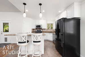 Kitchen featuring appliances with stainless steel finishes, a kitchen bar, white cabinets, decorative light fixtures, and a center island