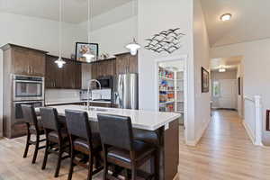 Kitchen with stainless steel appliances, dark brown cabinets, light countertops, light wood finished floors, and a breakfast bar