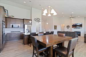 Dining room featuring high vaulted ceiling, a chandelier, light wood-style flooring, a glass covered fireplace, and a ceiling fan