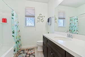 Full bath with healthy amount of natural light, vanity, shower / bath combo with shower curtain, and wood finished floors