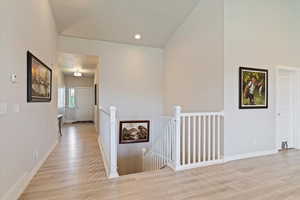 Corridor with an upstairs landing, light wood-type flooring, and recessed lighting