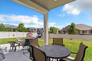 Fenced backyard featuring a playground, outdoor dining area, a patio area, a mountain view, and a residential view