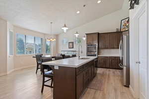 Kitchen with appliances with stainless steel finishes, a breakfast bar, dark brown cabinets, light countertops, and light wood-style flooring