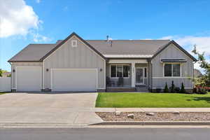 View of front of property with board and batten siding, an attached garage, a front yard, driveway, and covered porch