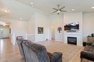 Living area with light wood-type flooring, a ceiling fan, a brick fireplace, high vaulted ceiling, and recessed lighting