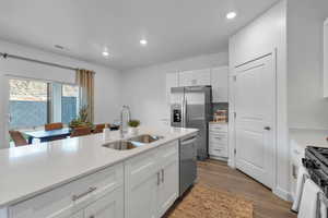 Kitchen with appliances with stainless steel finishes, white cabinets, light countertops, wood finished floors, and recessed lighting