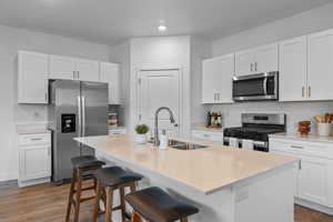 Kitchen featuring appliances with stainless steel finishes, dark wood-style flooring, a kitchen breakfast bar, an island with sink, and recessed lighting
