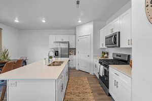 Kitchen featuring stainless steel appliances, recessed lighting, dark wood-style floors, white cabinets, and a kitchen breakfast bar